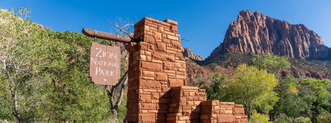 Zion National Park in Utah. Entrance sign at Pedestrian entrance to the iconic national park. The Watchman sandstone mountain summit. South entrance.