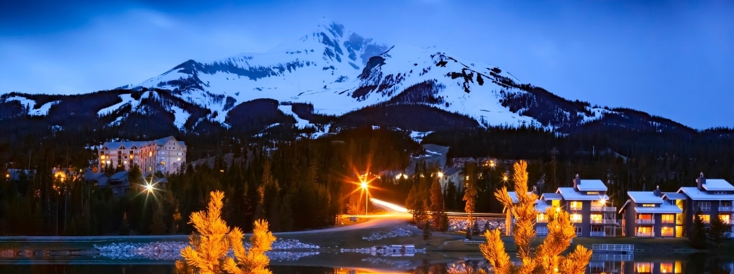 Big Sky Montana, United States, Big Sky Mountain Village ski resort on dusk, dwarfed by the enormity of Lone Mountain full of snow in the Madison Range, Montana USA. 